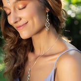 A woman with wavy brown hair smiles with closed eyes, wearing Kaora Sandara Jewelry's Quantum Shift NEW Sterling Silver with Crystal Gemstones (Size S), paired with matching earrings and a lavender top, in a sunlit outdoor setting.