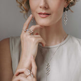 A woman poses with her hand near her chin, wearing a Kaora Sandara Jewelry Quantum Shift NEW Ring in sterling silver with chalcedony (size S) and other silver jewelry. She has softly curled hair and a sleeveless beige top.
