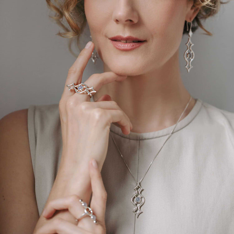 A woman poses with her hand near her chin, wearing a Kaora Sandara Jewelry Quantum Shift NEW Ring in sterling silver with chalcedony (size S) and other silver jewelry. She has softly curled hair and a sleeveless beige top.