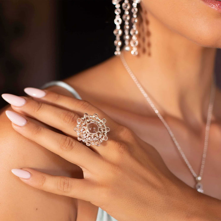 A woman with manicured nails wears the Kaora Sandara Jewelry Purity Ring—sterling silver with a central crystal, size S—paired with dangling earrings and a delicate necklace against her bare shoulder and neck.