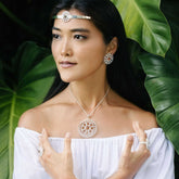 A woman poses before lush green leaves in an off-shoulder white top, wearing the Kaora Sandara Jewelry Purity Pendant—Sterling Silver with Crystal, Size L—from the Purity Collection.