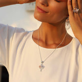 A woman in a white top smiles softly with her eyes closed, wearing Kaora Sandara Jewelry's Happy Parents Pendant in sterling silver with crystal, chalcedony, and rose quartz, plus matching earrings and ring as she touches her ear in warm natural light.