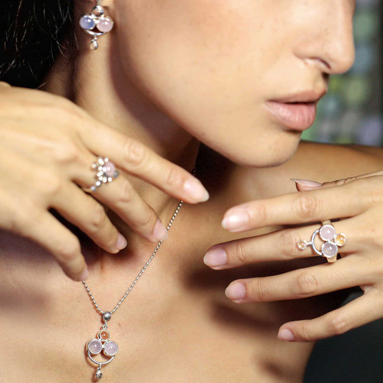 A woman elegantly wears Kaora Sandara Jewelry’s Happy Parents Earstuds in Sterling Silver with Crystal, Chalcedony, and Rose Quartz, her hands gracefully posed by her face and neck to highlight the jewelry.
