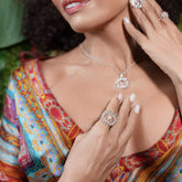 A woman in a colorful dress displays femininity as she showcases the Kaora Sandara Jewelry "Anima Ring"—Sterling Silver with Crystal & Rose Quartz—her manicured hands gently touching her chest and neck.