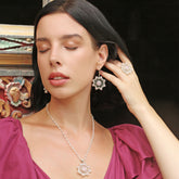 With her eyes closed, a woman in a deep pink dress touches her ear, showcasing Kaora Sandara Jewelry's Silver Earhooks Source of Love—crystal and rose quartz sterling silver earrings that complement her elegant style.