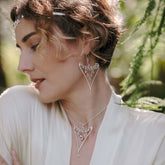 A woman with short, curly hair wears Kaora Sandara Jewelry’s Fifth Dimension Earhooks—Sterling Silver with Crystal Spheres. Dressed in a light, flowing top, she stands outdoors in gentle natural light.