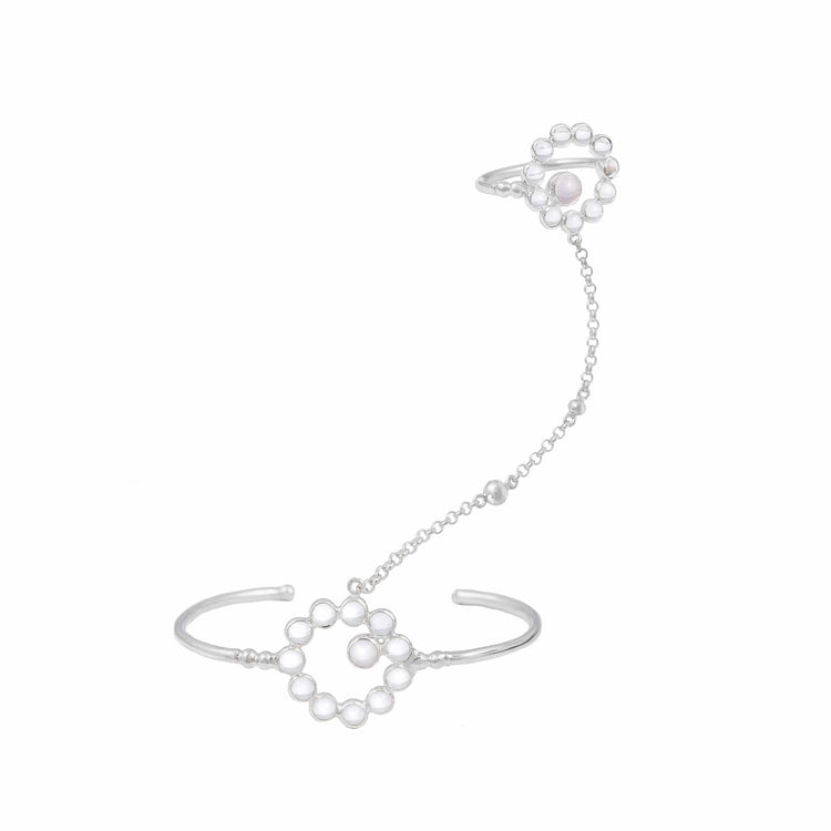 The Silver Hand Chain Me with Crystal & Rose Quartz by Kaora Sandara Jewelry connects a 925 silver cuff bracelet and ring with a delicate chain adorned with white pearls, rose quartz, and crystals in a floral design.