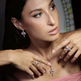 A woman with long dark hair wears Kaora Sandara Jewelry’s Happy Parents Ring—sterling silver with crystal, chalcedony, and rose quartz. She poses in a strapless pink top, hands near her neck, looking to the side.