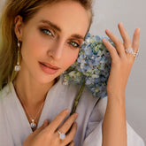 A woman with wavy blonde hair poses with a blue hydrangea, wearing the Kaora Sandara Jewelry Silver Pendant "I'M A Queen" with Chalcedony and a light, flowy top.