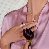 A woman in a pink satin robe holds a dark purple tulip and wears a silver necklace with a Rose Quartz pendant for universal love, plus Kaora Sandara Jewelry's Silver Ring Harmony with Rose Quartz Sphere Gemstones on her hand.