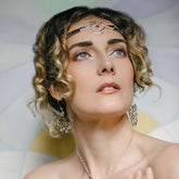 A woman with short, curly hair wears Kaora Sandara Jewelry’s Higher Self Earhooks—sterling silver adorned with crystal and chalcedony—as she gazes upward serenely against a soft pastel background.