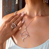 A woman wearing the Kaora Sandara Jewelry Magic Path Ring—Sterling Silver with Crystal Gemstones—and a matching silver necklace with circular designs, gently touches her necklace with pale pink manicured nails, dressed in a light top.