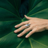 A hand adorned with the Kaora Sandara Jewelry Intuition Ring—Sterling Silver & Gold-Plated with Amethyst—rests on a large green tropical leaf, fingers gently splayed across its surface.