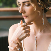 A woman with curly hair gazes thoughtfully, radiating tranquility as she wears Kaora Sandara Jewelry’s Silver Earhooks State—elegant earrings adorned with crystal and chalcedony gemstones in delicate circular settings.