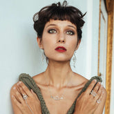 A woman with short dark hair and bangs wears the Kaora Sandara Jewelry Silver Pendant Beyond Fears on a thin 45cm square chain with crystal, paired with dramatic eye makeup, red lipstick, and an off-shoulder green top.