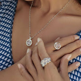 A woman in a blue and white dress models Kaora Sandara Jewelry: the Silver Ring The Dance with Chalcedony, two rings and a pendant necklace, each set with round chalcedony stones. Her nails are light and neatly manicured.