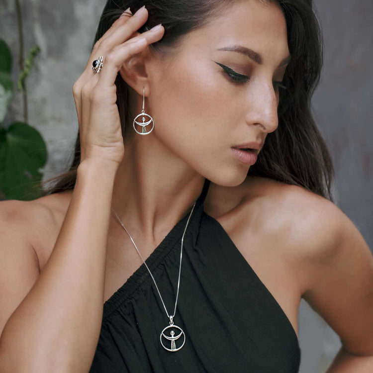 A woman in a one-shoulder black top wears Kaora Sandara Jewelry’s Releasing From the Deepest Fears Earhooks—Sterling Silver 925, Size S—and matching geometric necklace and ring. She looks down, thoughtfully touching an earring.