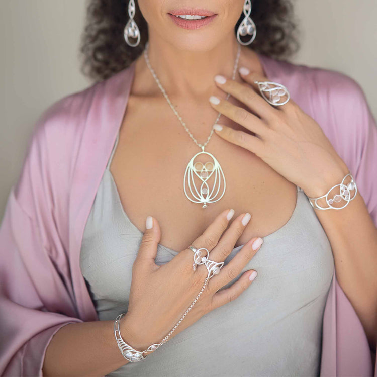 A woman models the Kaora Sandara Jewelry Silver Hand Chain Transition Gift, featuring intricate silverwork with rose quartz sphere gemstones that evoke spiritual love and serenity, her hands gracefully posed to highlight the accessory.