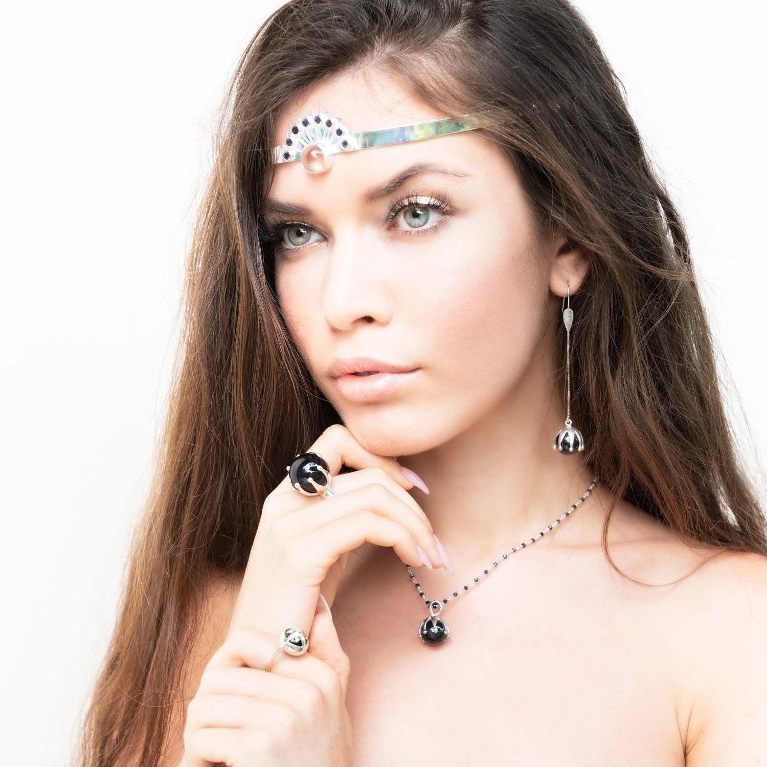 A woman with long brown hair wears the Kaora Sandara Jewelry Silver Ring I'M A Queen with Black Agate (Size M), styled with sterling silver jewelry, against a plain white background. She gazes slightly left, her expression soft.