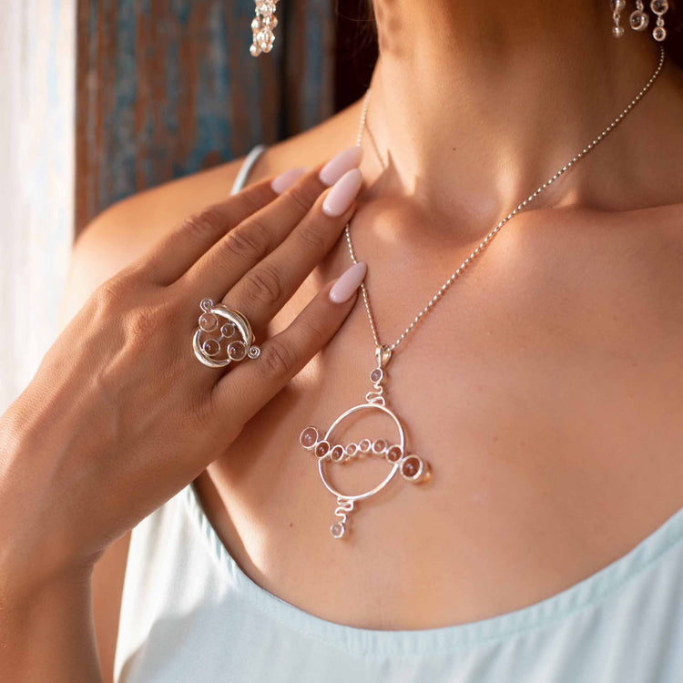 A woman in a light blue sleeveless top displays her pale pink manicured nails, showcasing the Kaora Sandara Jewelry Soul Potential Pendant—Sterling Silver with Crystal & Chalcedony—featuring intricate circular designs.