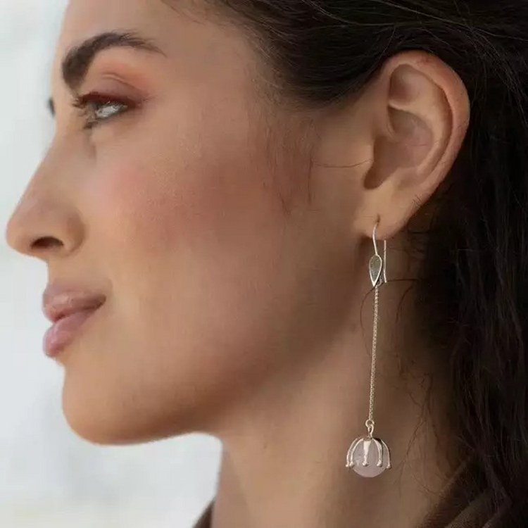 A woman in profile wears Kaora Sandara Jewelry's I'M A Queen Earhooks—sterling silver earrings with teardrop studs and dangling rose quartz beads. Her dark hair is tucked back, accentuating her makeup and smooth skin.