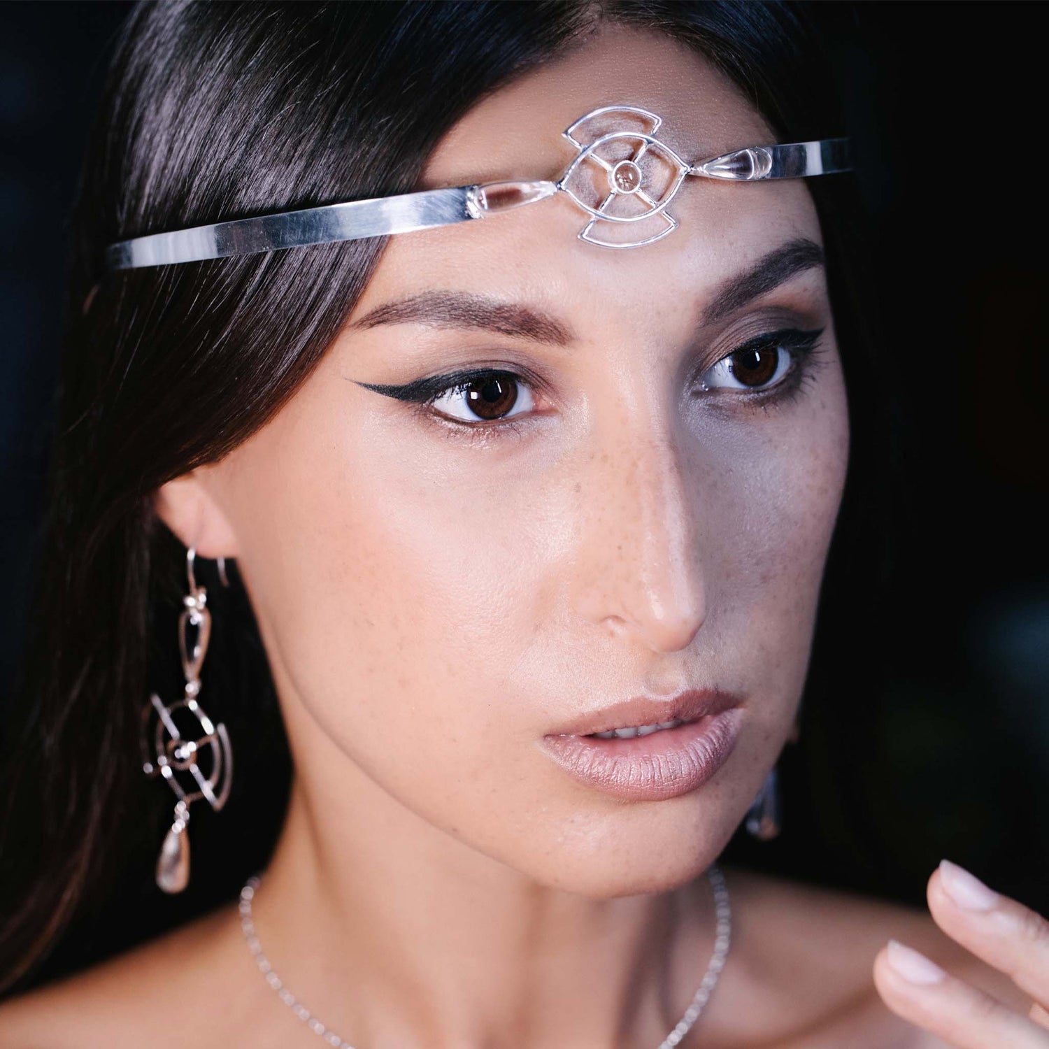 A woman with long dark hair wears the Soul Guidance Headband—Sterling Silver with Crystal—from Kaora Sandara Jewelry. With winged eyeliner and nude lipstick, she gazes slightly to the side against a dark background.