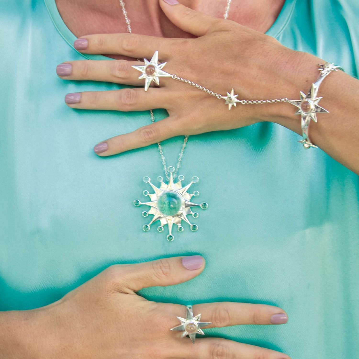 A person wears the Kaora Sandara Jewelry Silver Hand Chain Magic Star, featuring star motifs and crystal sphere gemstones that inspire intuition, posing with hands on a shiny turquoise top.