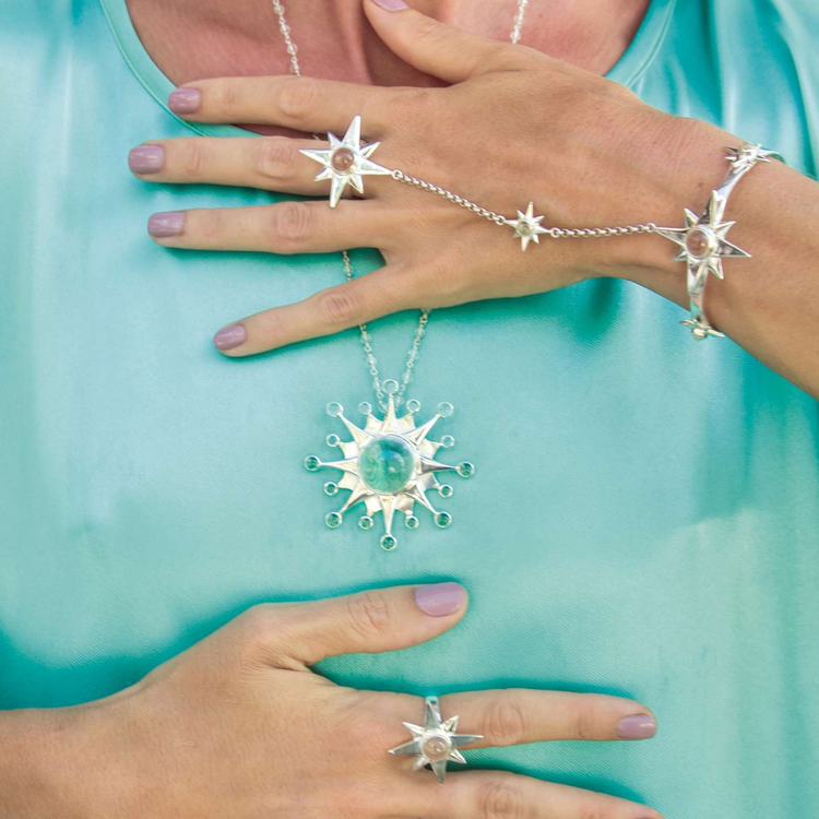 A person wears the Kaora Sandara Jewelry Silver Hand Chain Magic Star, featuring star motifs and crystal sphere gemstones that inspire intuition, posing with hands on a shiny turquoise top.