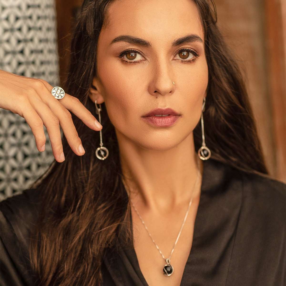 A woman with long brown hair wears a black top and Kaora Sandara Jewelry's Silver Earhooks The Wave with Black Agate Spheres gemstones. She gazes calmly and confidently at the camera.