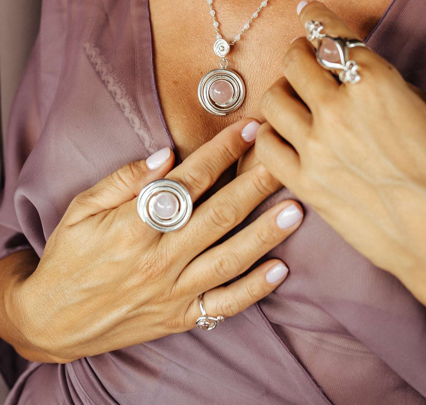 A person in a sheer mauve top showcases Kaora Sandara Jewelry’s Silver Ring Open Spiral with Rose Quartz (Size M) alongside matching pieces, all accented by pale pink nails—radiating unconditional love.