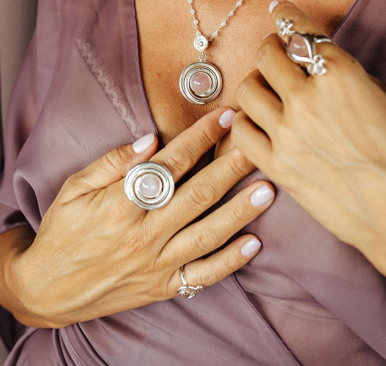 A person in a sheer mauve top showcases Kaora Sandara Jewelry’s Silver Ring Open Spiral with Rose Quartz (Size M) alongside matching pieces, all accented by pale pink nails—radiating unconditional love.