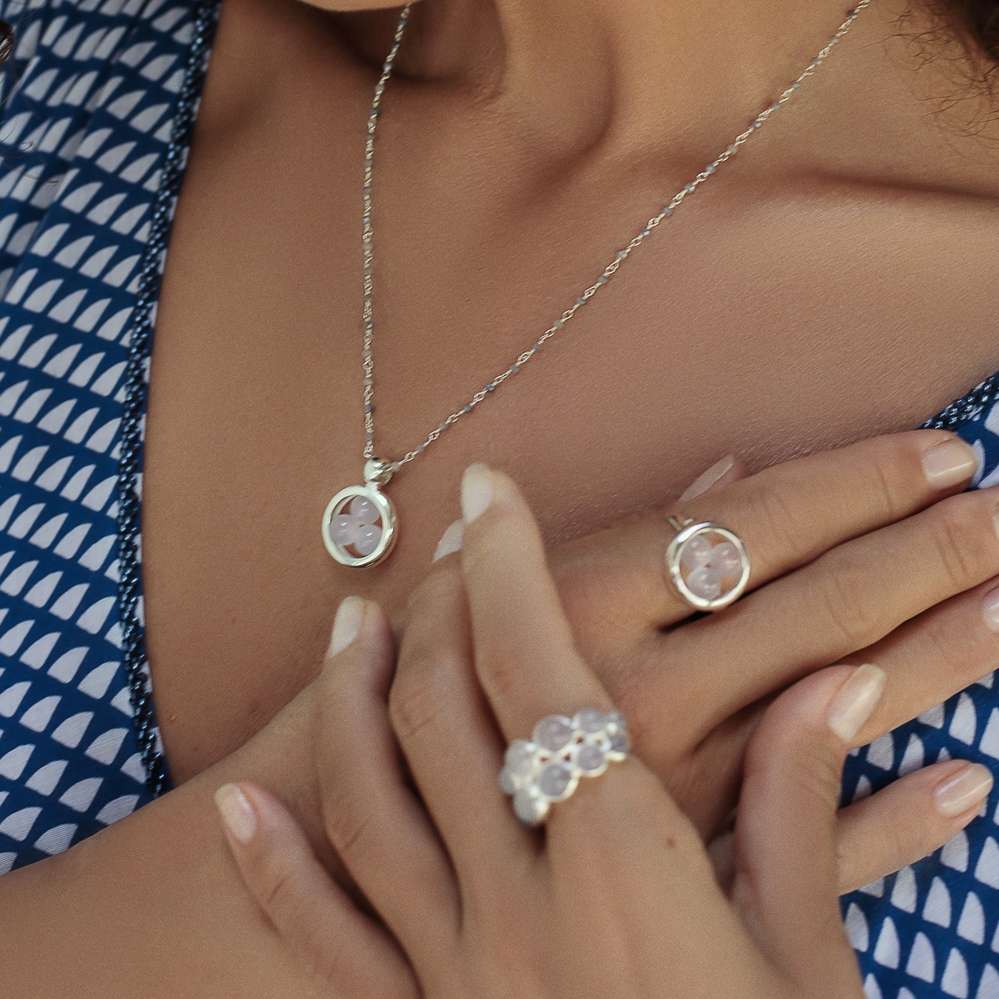 A woman in a blue and white dress models Kaora Sandara Jewelry: the Silver Ring The Dance with Chalcedony, two rings and a pendant necklace, each set with round chalcedony stones. Her nails are light and neatly manicured.
